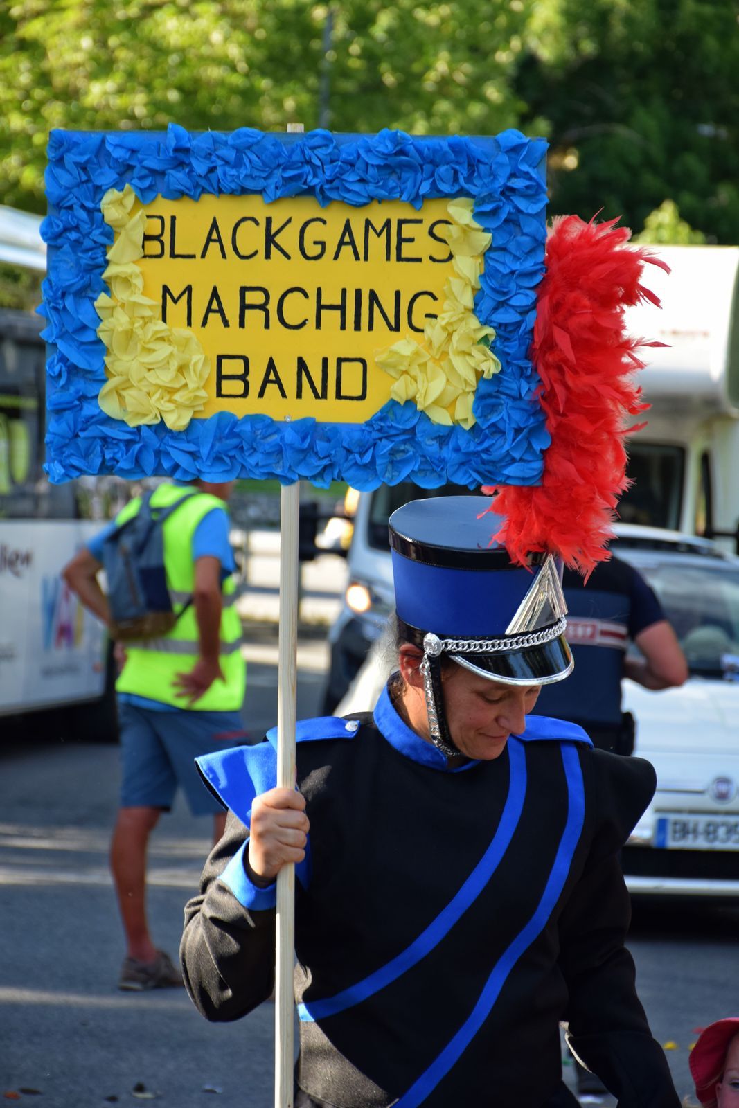 Angélique, porte-drapeau des Blackgames, tient la pancarte « Blackgames Marching Band » lors du Corso Fleuri de l’Embrunais